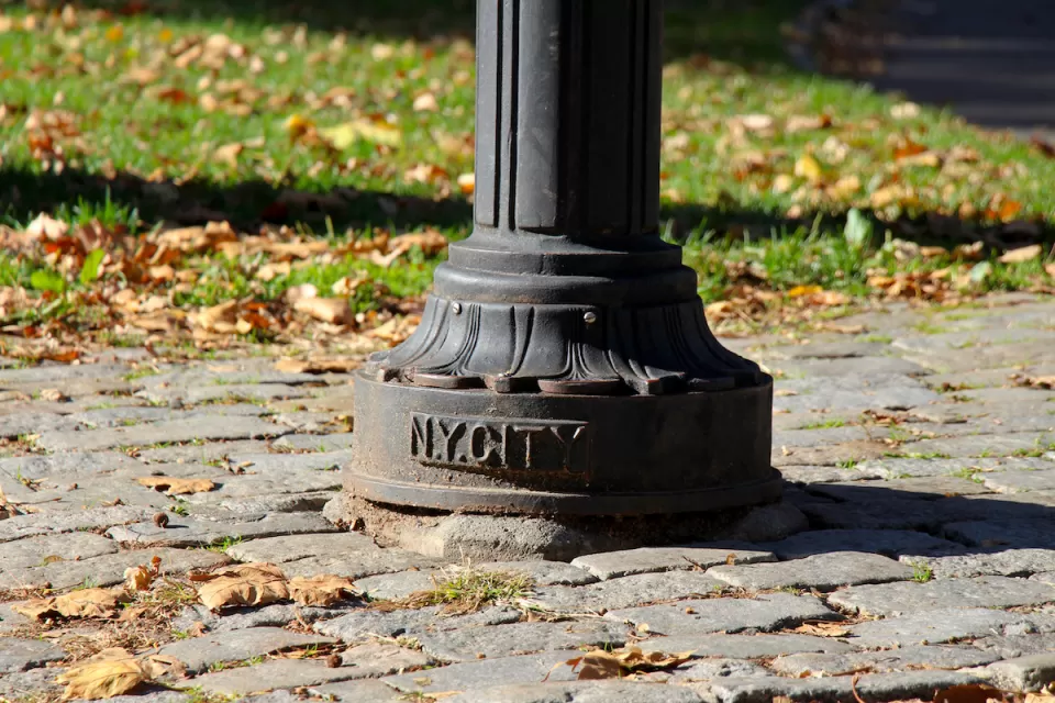 CLose-up of bottom of lamp post with NY CITY plaque on cobblestone sidewalk in Central Park, New York City.